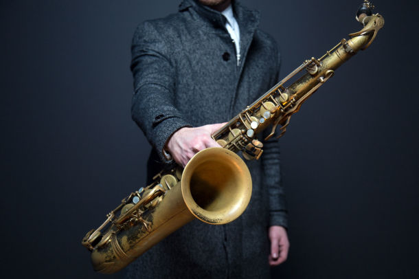 Man in suit holding a tenor saxophone in his hand; rent tenor saxophones first