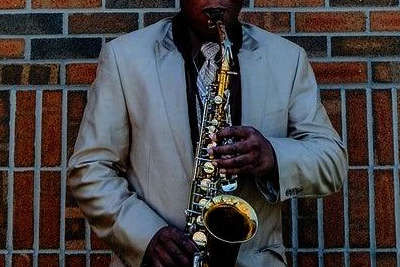 Man playing alto sax in from of brick wall; rent alto saxophones here